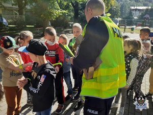 policjant rozdaje dzieciom opaski odblaskowe, stoją na boisku