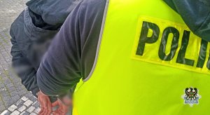 policjant prowadzi zatrzymanego młodocianego, który ma ręce zapięte kajdankami