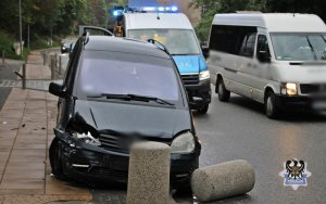 Na zdjęciu widać pojazd uszkodzony w zdarzeniu drogowym i w tle radiowóz z włączonymi sygnałami błyskowymi