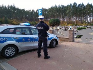 policjant stoi przy radiowozie przed cmentarzem