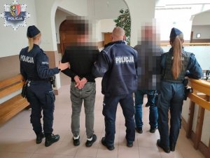 zatrzymane osoby stojące z policjantami w budynku Komendy