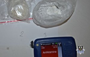 dwa worki z białym proszkiem leżą na blacie, poniżej tester narkotykowy z napisem Amfetamina na wyświetlaczu