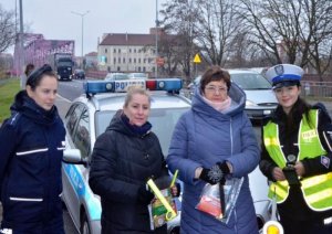 policjantki z kobietami trzymającymi gadżety profilaktyczne stoją przy drodze obok samochodu