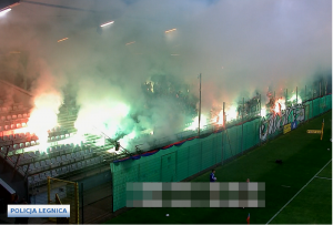 Na zdjęciu widać moment palenia się rac świetlnych i dymnych na trybunach stadionu w Legnicy