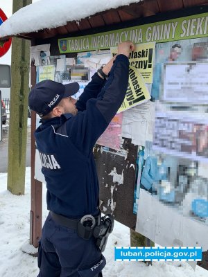 Policjant zawiesza na tablicy ogłoszeń ulotkę profilaktyczną dotyczącą odblasków
