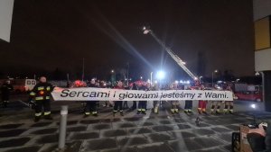 strażacy trzymają transparent z napisem sercami i głowami jesteśmy z wami