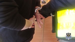 kajdanki zakładane przez policjanta w kamizelce na ręce mężczyzny