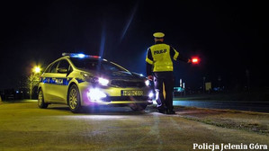 Policjant stoi po zmierzchu obok radiowozu z włączonymi światłami błyskowymi