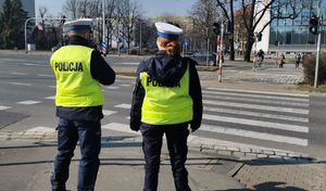 Policjanci stoją przy przejściu dla pieszych i obserwują zachowania uczestników ruchu drogowego