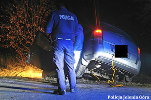 pora nocna, tył pojazdu wystający z przydrożnego rowu, stojący na jezdni policjant