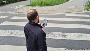 mężczyzna trzymający telefon w ręku przed przejściem dla pieszych