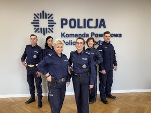 Sześcioro policjantów stoi obok ściany z napisem POLICJA i policyjnym logo