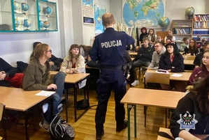 policjant prowadzi spotkanie z uczniami, młodzież siedzi w ławkach w klasie