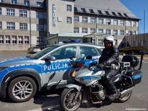 policjant siedzi na motocyklu, w tle widać budynek komendy i radiowóz