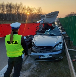 policjant stoi przy rozbitym samochodzie uczestniczącym w zdarzeniu drogowym