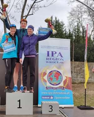 policjanci biorący udział w biegach stoją na podium trzymając w rękach puchary i medale i dyplomy