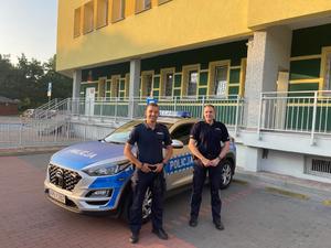 dwóch umundurowanych policjantów stojących koło radiowozu