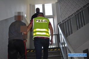 policjanci prowadzą zatrzymanego mężczyznę schodami do góry budynku