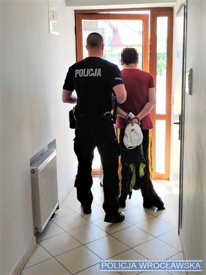 Policjant stoi wraz z zatrzymanym przy drzwiach