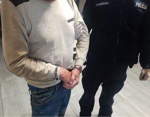Policjant stoi z zatrzymanym mężczyzną, który ma na rękach założone kajdanki