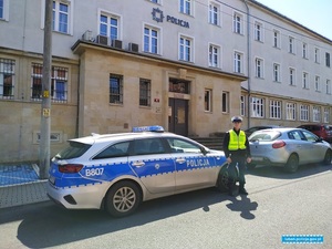 Policjant stoi obok radiowozu, w tle budynek