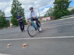 Uczeń jedzie na rowerze po przeszkodzie, obok stoi policjant