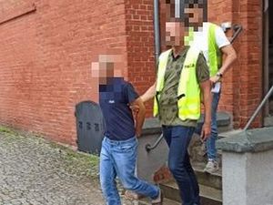 prowadzenie zatrzymanego mężczyzny przez policjantów w kamizelkach