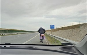 Zdjęcie przedstawia rowerzystę poruszającego się pasem awaryjnym drogi ekspresowej