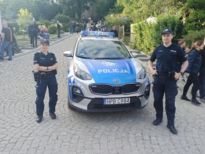 policjanci stoją przy radiowozie na terenie miasta