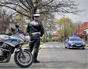 Zdjęcie przedstawia policjanta przy motocyklu oraz radiowóz