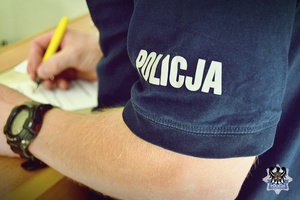 Zdjęcie przedstawia policjanta wypełniającego dokumentację procesową