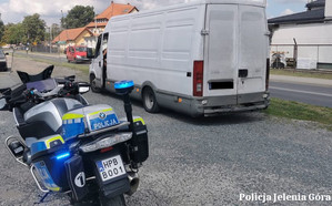 Zdjęcie przedstawia policyjny motocykl oraz zatrzymany do kontroli pojazd dostawczy