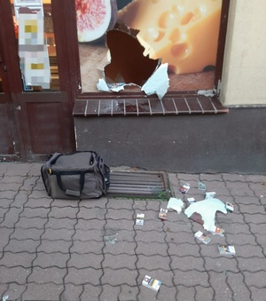 Na zdjęciu widać wybitą witrynę sklepową i kilka paczek papierosów leżące na chodniku