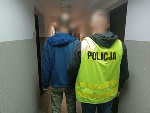 policjant prowadzi zatrzymanego mężczyznę, na biurku leżą zabezpieczone przedmioty