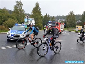 Na drodze widać trzy jadące rowery, radiowóz policyjny, straż oraz w tle drzewa