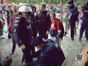 policjant w umundurowaniu służbowym zakłada młodemu chłopakowi strój ochrony indywidualnej nieetatowego oddziału policji