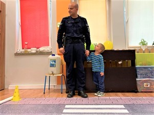 Policjant z przedszkolakiem podczas przechodzenia przez matę z przejściem dla pieszych