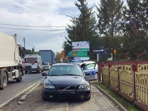 Czarny samochód stojący wzdłuż na chodniku, w tle radiowóz, po lewej stronie stojące samochody