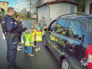 Dzieci w kamizelkach odblaskowych wraz z policjantem podczas kontroli drogowej