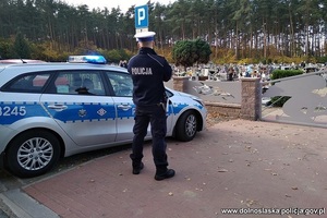 Umundurowany policjant na tle radiowozu i cmentarza
