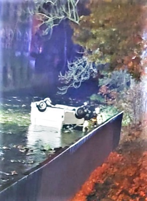 Zdjęcie przedstawia biały samochód leżący na dachu w rzece