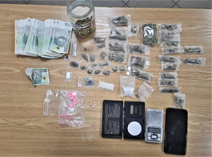 Zdjęcie przedstawia zabezpieczoną gotówkę, opakowania z narkotykami, telefon oraz wagę