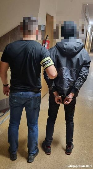 Zdjęcie przedstawia policjanta oraz zatrzymanego mężczyznę z założonymi na ręce kajdankami