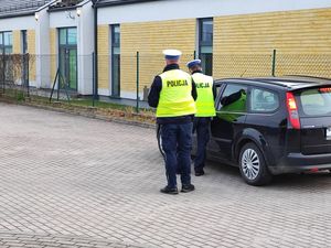 dwaj policjanci w mundurach i kamizelkach odblaskowych stoją przy zaparkowanym samochodzie