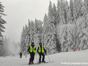 Dwie osoby w kamizelkach odblaskowych, na nartach stoją na dworze w śnieżnym otoczeniu