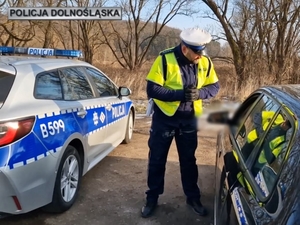 Policjant stojący koło radiowozu, kontroluje kierowcę w samochodzie osobowym.