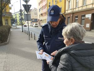 na dworze przy drodze policjantka w mundurze wręcza ulotkę starszej kobiecie