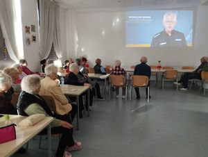 w pomieszczeniu policjantka w mundurze stoi przed grupą osób