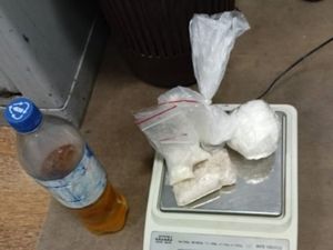 na podłodze stojąca butelka z brązową substancją, a po prawej leżące na blacie wagi woreczki z białą substancją