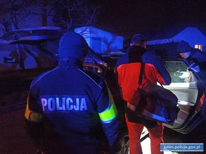 Na zdjęciu policjant i ratownik medyczny stojący koło samochodu.
